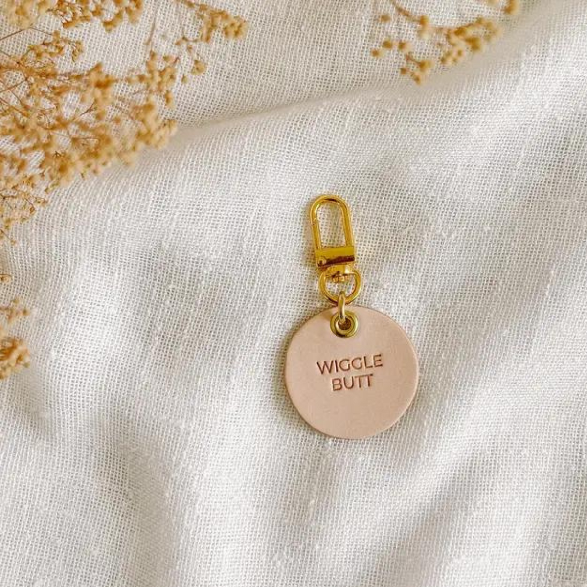 Vegetable tanned leather dog tag with brass hardware that says "Wiggle Butt"