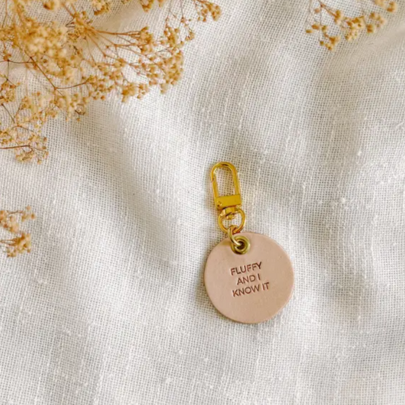 Vegetable tanned leather dog tag with brass hardware that says "Fluffy And I Know It"